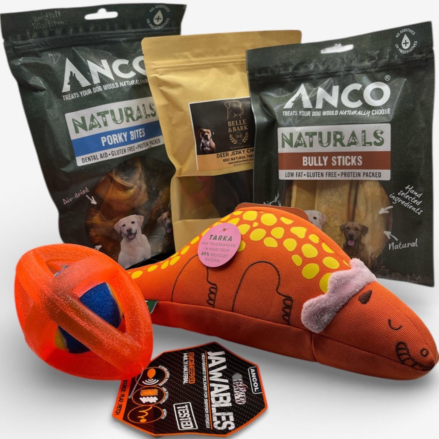 Dog toys and treats including a plush fish toy, a ball, and packages of Anco Naturals and Bella & Co. products on a white background.